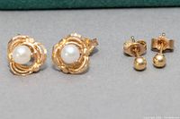 Two pairs of stud earrings on flat surface, one with cultured pearls and decorative 10K gold setting, the other with plain 10K gold balls.