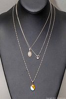 Three sterling silver necklaces displayed on black bust, showing chains and pendants including religious, heart, and multicolored stone motifs.