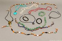 All jewelry items displayed laid flat on a white surface showing variety of necklaces and bracelets with different stone beads in multiple colors.