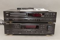 Front view of Denon CD player model DCD-615 on top of stereo receiver model DRA-365R, showing power cables, remote, and manuals on top.