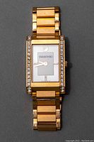 Front view of rose gold toned Swarovski rectangular watch with crystal accents and white face.