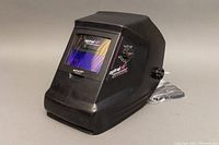 Front and left side view of the black Optrel Solarmatic Comfort welding helmet showing the viewing window, the adjustable side knob, and the overall helmet shape.