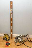 Wooden 4-foot leveler standing upright alongside two Black & Decker circular saws on floor