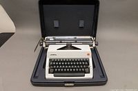 Vintage Olympia manual typewriter shown inside its hard carrying case with lid open.