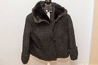 Front view of the black curly Persian lamb fur swing jacket with large dark fox fur collar, displayed on a dress form.