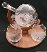 Globe-shaped glass decanter with etched world map mounted on wooden stand with leather straps, with two stemless glasses etched with world maps.