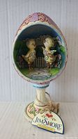 Front view of the egg-shaped Jim Shore figurine showing the two decorative chicks inside, pedestal stand, and Jim Shore tag.