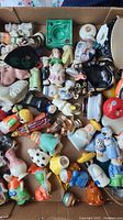 Box of varied single salt and pepper shakers including animal and figurine shapes in multiple colors and designs.