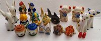 Photo shows various vintage salt and pepper shakers arranged in a single row. Includes white goats, children figures, pig faces, tall cats with spots, round shakers, houses, and buffalo figures.