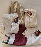 Photo of seven vintage women's clothing items laid out, showing tags and different styles including pants, tops, and sweaters.