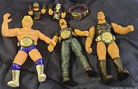 Three vintage wrestling figures shown with championship belts and separate arms accessory.