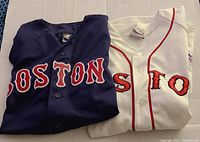 Folded navy blue and white Boston Red Sox jerseys showing front logos