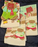 Set of kitchen towels and potholder showing gingerbread man chef, gingerbread house and festive holiday motifs, with tags attached indicating brand