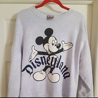 Front view of the light-colored vintage Disneyland sweatshirt with large Mickey Mouse graphic and 'Disneyland' text across the chest.