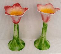 Two ceramic flower-shaped candle holders shown upright, highlighting the green leafy stems and colorful petals