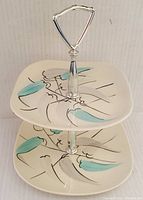 Front angled view showing both tiers of the platter with teal and gray leaf decoration and metal handle on top.