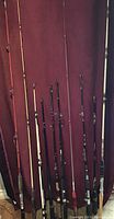 Full view of lot containing 10 fishing rods of different colors and styles leaning against a dark curtain