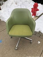 Front-facing view of a vintage green swivel tub office chair with castors on a chrome four-leg base, showing original upholstery and a separate seat cushion.