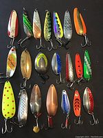 Photo showing full lot of 21 different fishing spoon lures arranged in rows, showcasing varied colors, sizes, shapes, and hook types.
