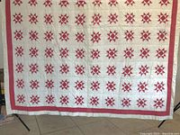 Full view of the quilt showing a white background with multiple red star blocks arranged in rows and columns, and a red bordering edge.
