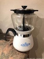Corning Ware coffee maker with ceramic pot base featuring blue floral pattern, clear glass upper bowl, black plastic handle, and metal lid