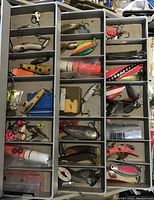 Top view of a multi-compartment tackle box filled with assorted fishing lures such as crankbaits, spoons, jigs, and plastic baits varied colors and sizes.