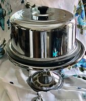 View of the assembled cake stand set with chrome dome cover on glass plate and pedestal base.