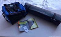 Photo showing the blue cooler bag, black cylindrical carrying bag, and folded reference sheet for the camping mattress.