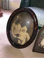 Front view of the ovular wood photo frame with glass dome showing sepia photo of woman and baby.