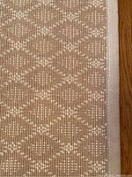 Close-up of the taupe area rug with diamond pattern showing the weave and edge binding.