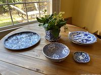 Photo of ceramic tray, plates, bowl, small dish with blue floral patterns and potted plant on wooden table near window