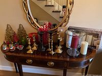 Full view of the lot from front showing all candlesticks, candles, and hurricane lamp placed on a brown wooden table with a decorative mirror on the wall behind.