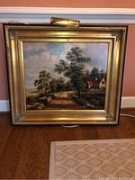 Front view of the farmhouse painting resting against a wall, showing the full artwork and frame.