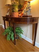 Full view of wooden foyer occasional table with decorative items on top and potted fern below.