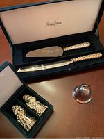Photo of boxed cake server and knife with decorative gilded handles alongside the bell and Santa shakers.