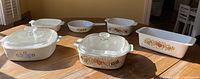 Photo showing five Corning Ware casserole dishes in various sizes and shapes with La Marjolaine and other floral patterns, two dishes have glass lids.