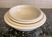 Stack of four white ceramic bowls nested inside each other on a kitchen counter with tiled backsplash
