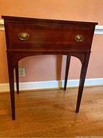 Front view of wooden accent table showing single drawer with brass oval pulls and tapered legs