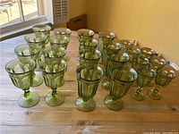 Photo showing 24 vintage green glassware pieces arranged on a wooden table illuminated by natural light.
