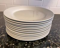 Stack of 12 white dinner plates showing edges and thickness