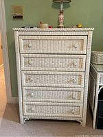 White wicker dresser with five drawers and clear knob handles against a green wall