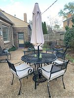 Round mesh-top dining table with center umbrella and four cushioned wrought-iron chairs on patio