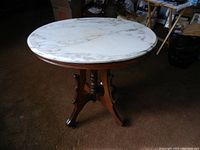 Oval white marble top accent table with medium-toned wooden base and brass wheels, shown in room setting.