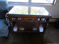 Front view of wood accent table showing drawer, glass top, and claw and ball wheels