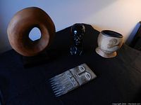 Four African inspired decorative pieces arranged on black cloth: circular wooden sculpture, small bust, cylindrical container, and carved comb.