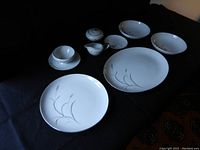 Multiple plates, bowls, covered sugar bowl, cream pitcher, and gravy boat displayed together featuring white china with subtle wheat spray design.