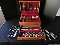 Full view of storage box containing assorted flatware and serveware. Items laid out including spoons, forks, knives, napkin rings and metal skewers.