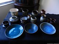Entire lot of 19 handmade pottery pieces including assorted vases and plates in various colors and textures on a black cloth surface