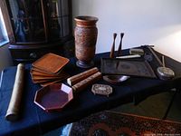 Photo showing assortment of wooden decorative items including trays, boxes, vases, and utensils arranged on a table with dark cloth