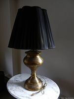 Full view of the brass table lamp with black pleated shade placed on a marble table, showing the lamp's entirety and design details on the base.